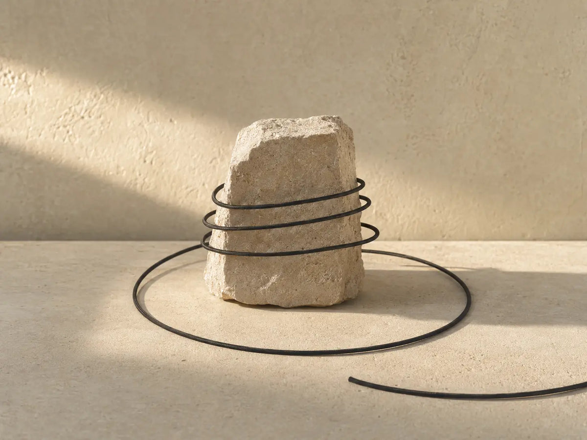 Black cord looping around a limestone anchor, representing repetitive thoughts after a relationship ends