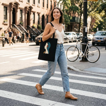 Woman carrying THE LISTENING black cotton art tote while walking along a sunlit city street.