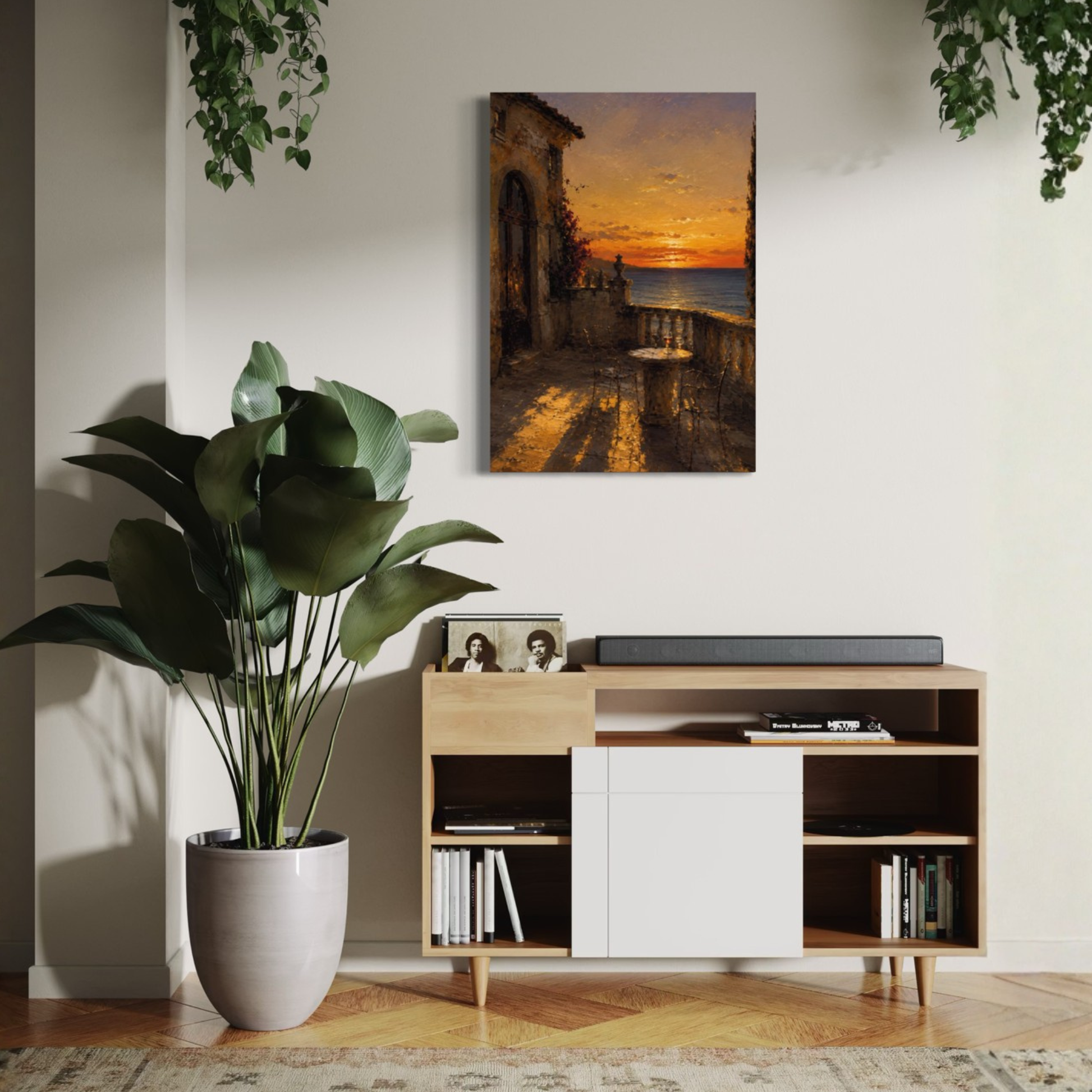 The Hour Mediterranean canvas art displayed on a white wall above a modern wooden and white media console. The room is styled with a large potted green plant on the left, hanging greenery at the top corners, and a patterned rug on the floor.