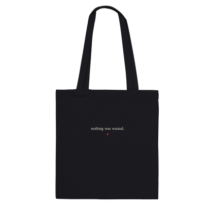 Back of THE MENDING black cotton tote featuring “nothing was wasted.” in small ivory serif lettering.