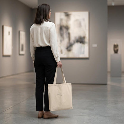 Rear view of a woman carrying THE THRESHOLD natural cotton tote through a contemporary art gallery.
