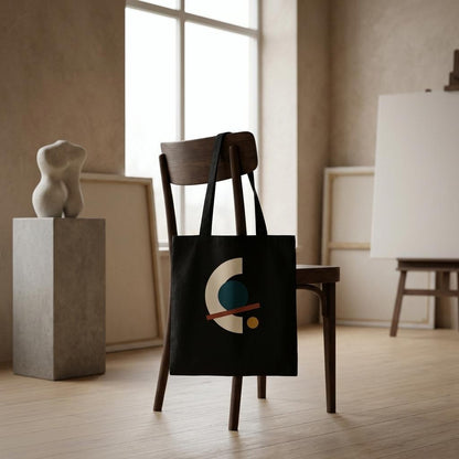 THE ALIGNMENT black cotton art tote hanging from a dark chair in a calm neutral interior.