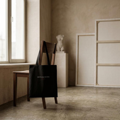 THE BLOOM black art tote displayed on a wooden chair in a neutral studio interior